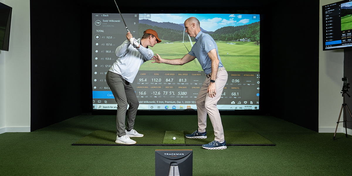 trainer working with a client while swinging on a golf simulator