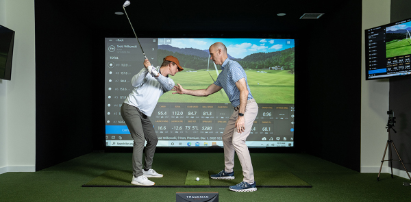 trainer coaching a client on the golf simulator