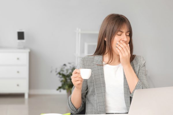 woman yawning and holding coffee